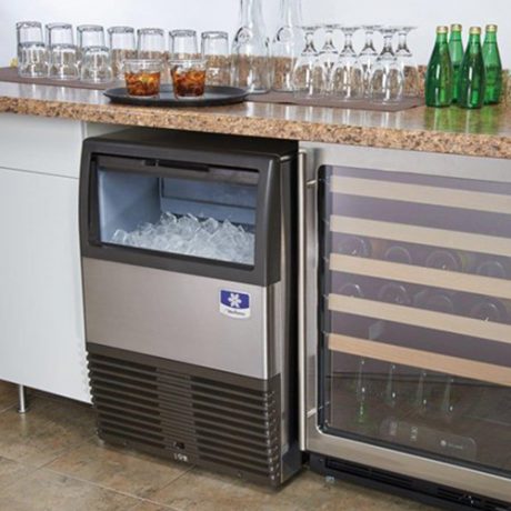 commercial undercounter Ice maker and wine cooler on a kitchen counter with glasses and bottles in the background.